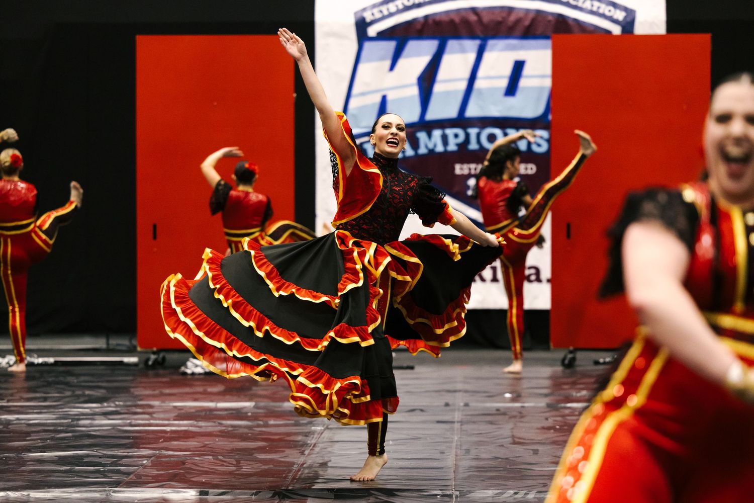 Young dancers in red and black flamenco costumes perform energetically on stage at a KID Champions dance competition.