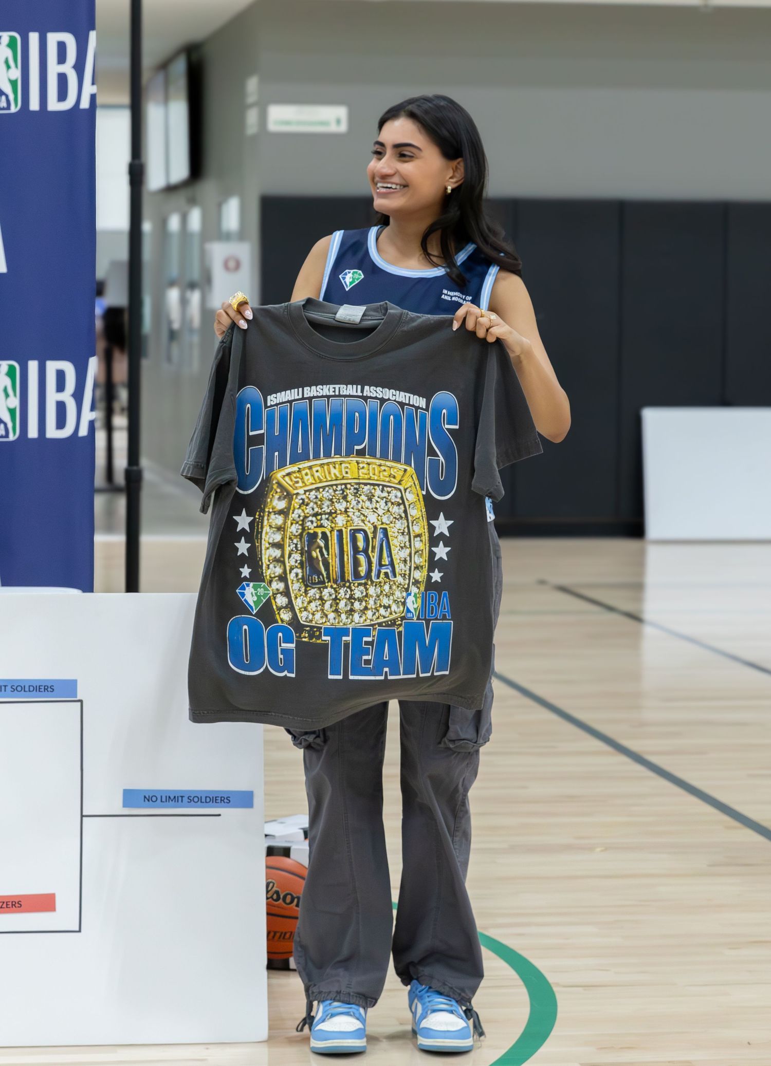 Person holding up a commemorative IBA Champions All-Star team t-shirt in a basketball court.