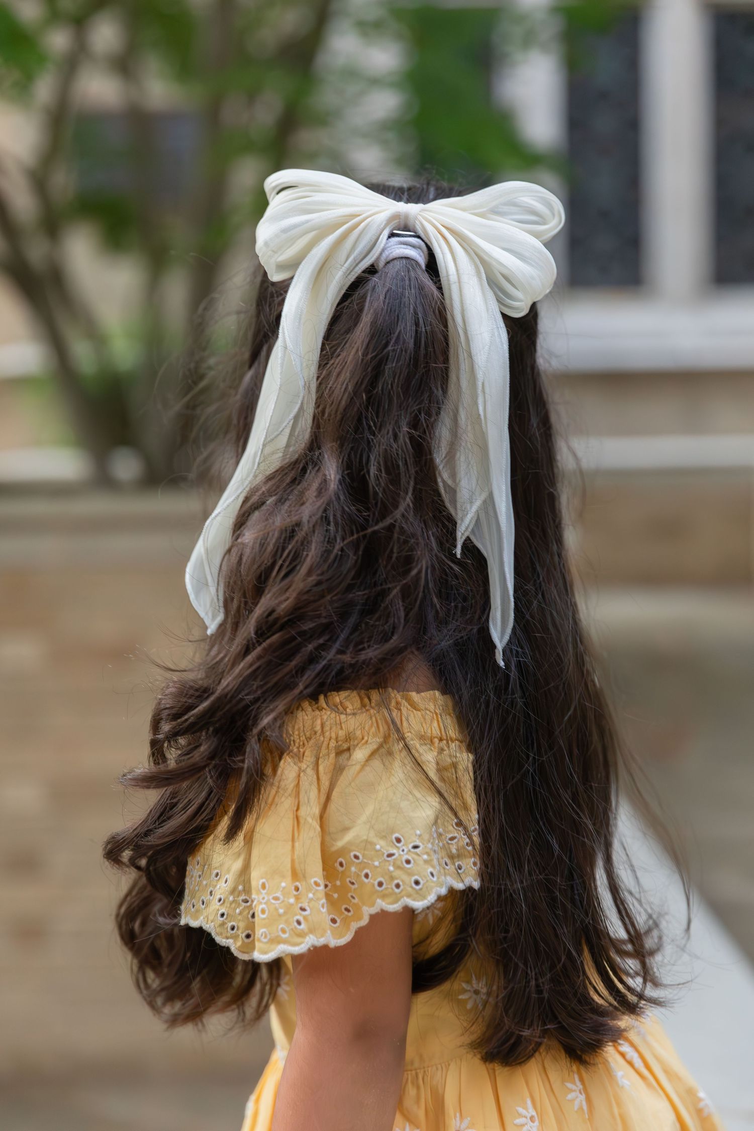 Back view of long dark hair with white bow accessory against brick wall background.