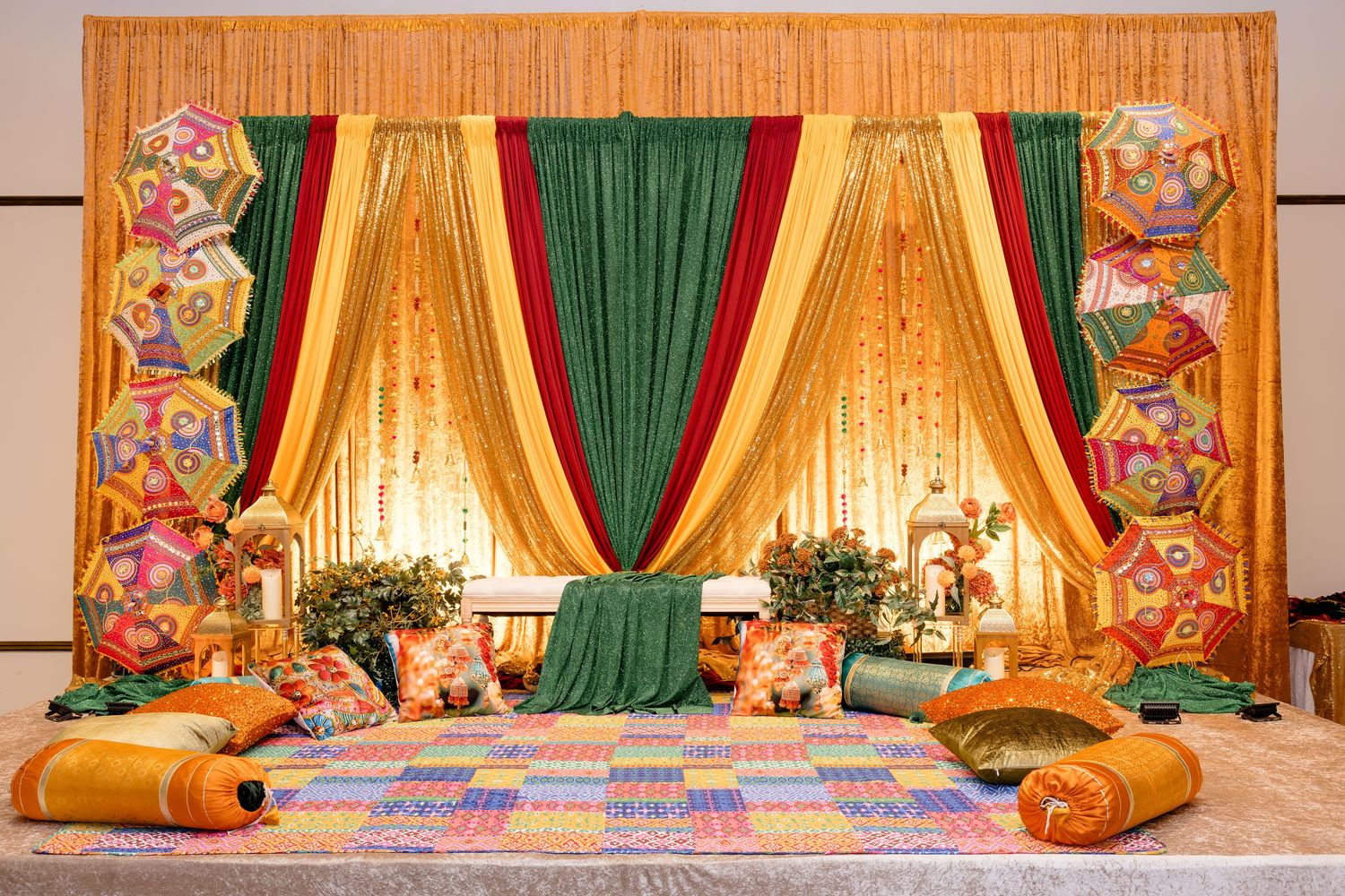 Vibrant Mehndi stage decor with colorful cushions, green and gold drapes, and festive kite decorations.