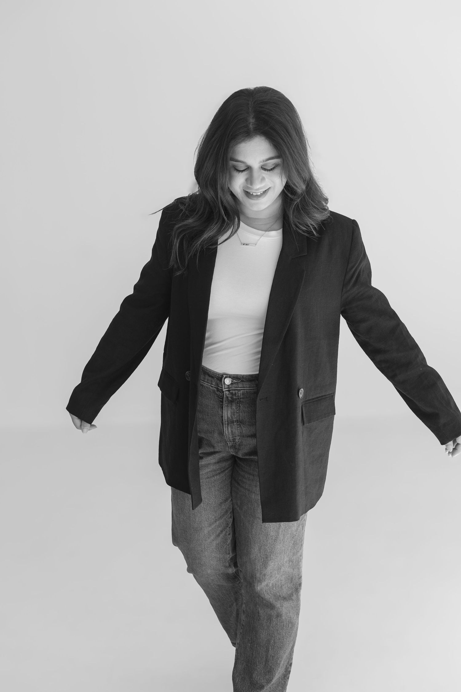 Black and white photo of person in blazer and jeans striking casual pose against white backdrop.