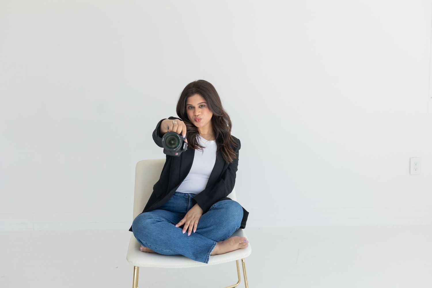Business professional in casual attire sitting cross-legged on chair in studio setting.