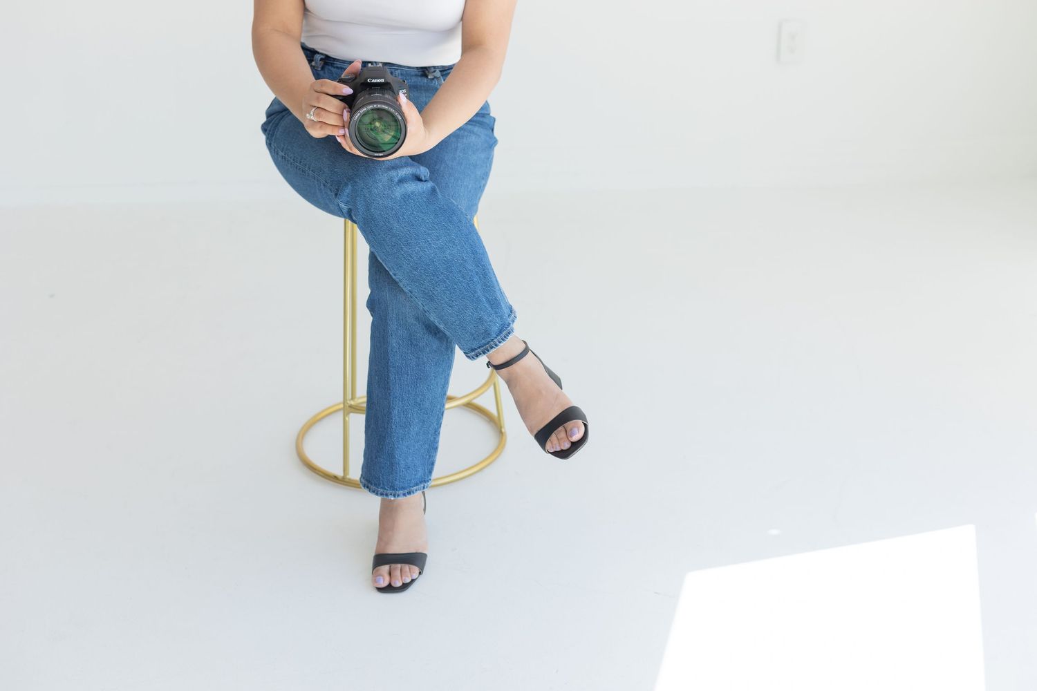 Cropped view of photographer in blue jeans sitting on stool holding camera.