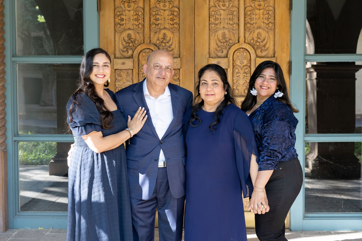 Family of four posing together in coordinating navy blue outfits in front of an ornate wooden door.