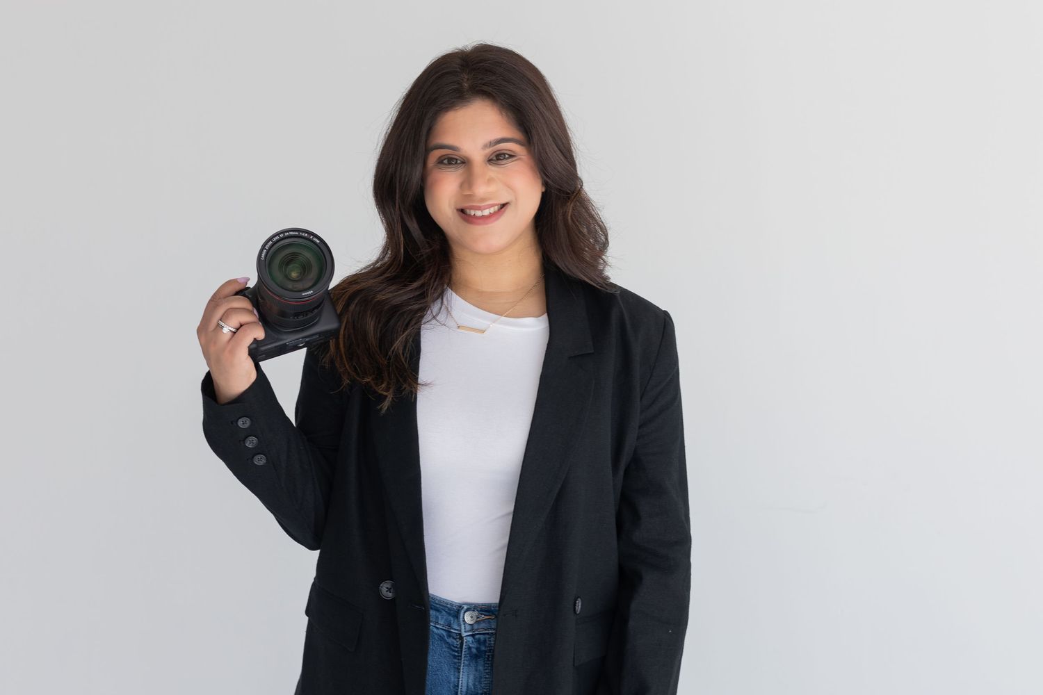 Professional photographer holding a camera while wearing a black blazer against white background.