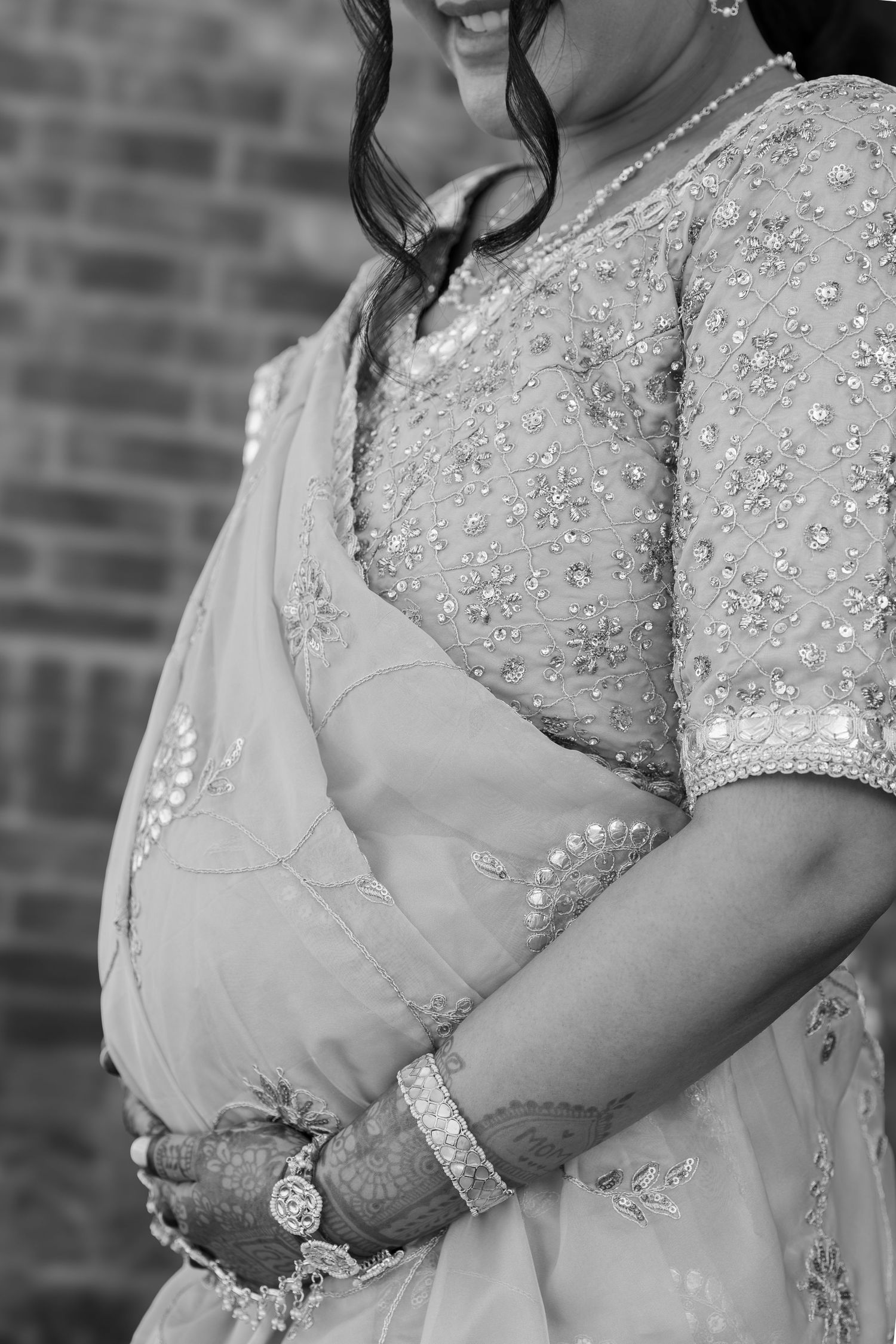 Close-up details of an elegant beaded wedding dress with sheer fabric and intricate embellishments against a brick wall.