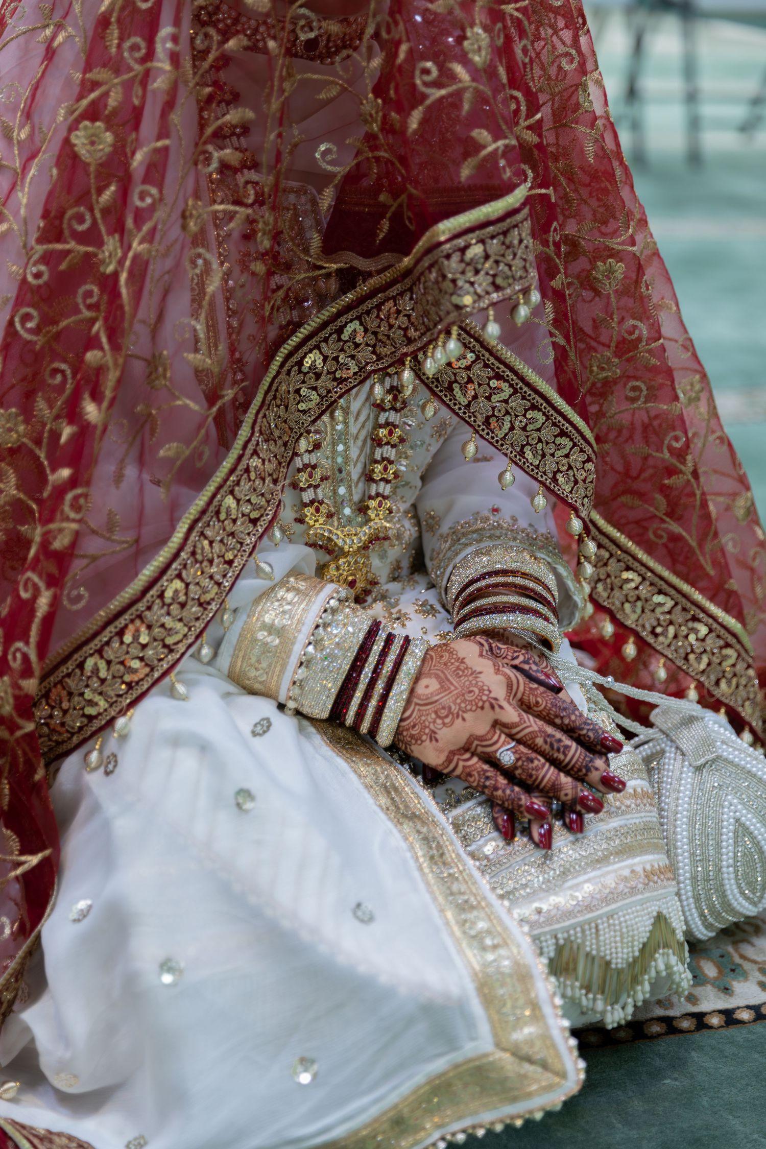 Traditional bridal attire with detailed henna and bangles on hands resting on ornate red and gold lehenga.
