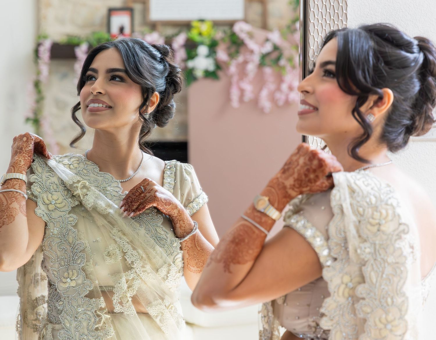A bride in light-colored traditional outfit showing her henna-decorated hands while getting ready.