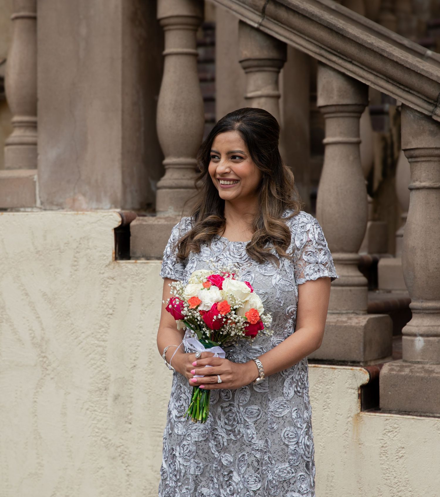 Person in a sparkly silver dress holds a vibrant bouquet of flowers while standing by stone columns.