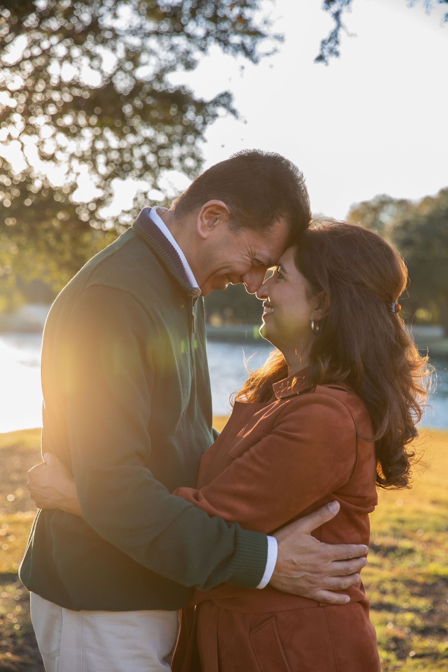 Romantic couple embracing at sunset by a lake with golden sunlight filtering through trees.