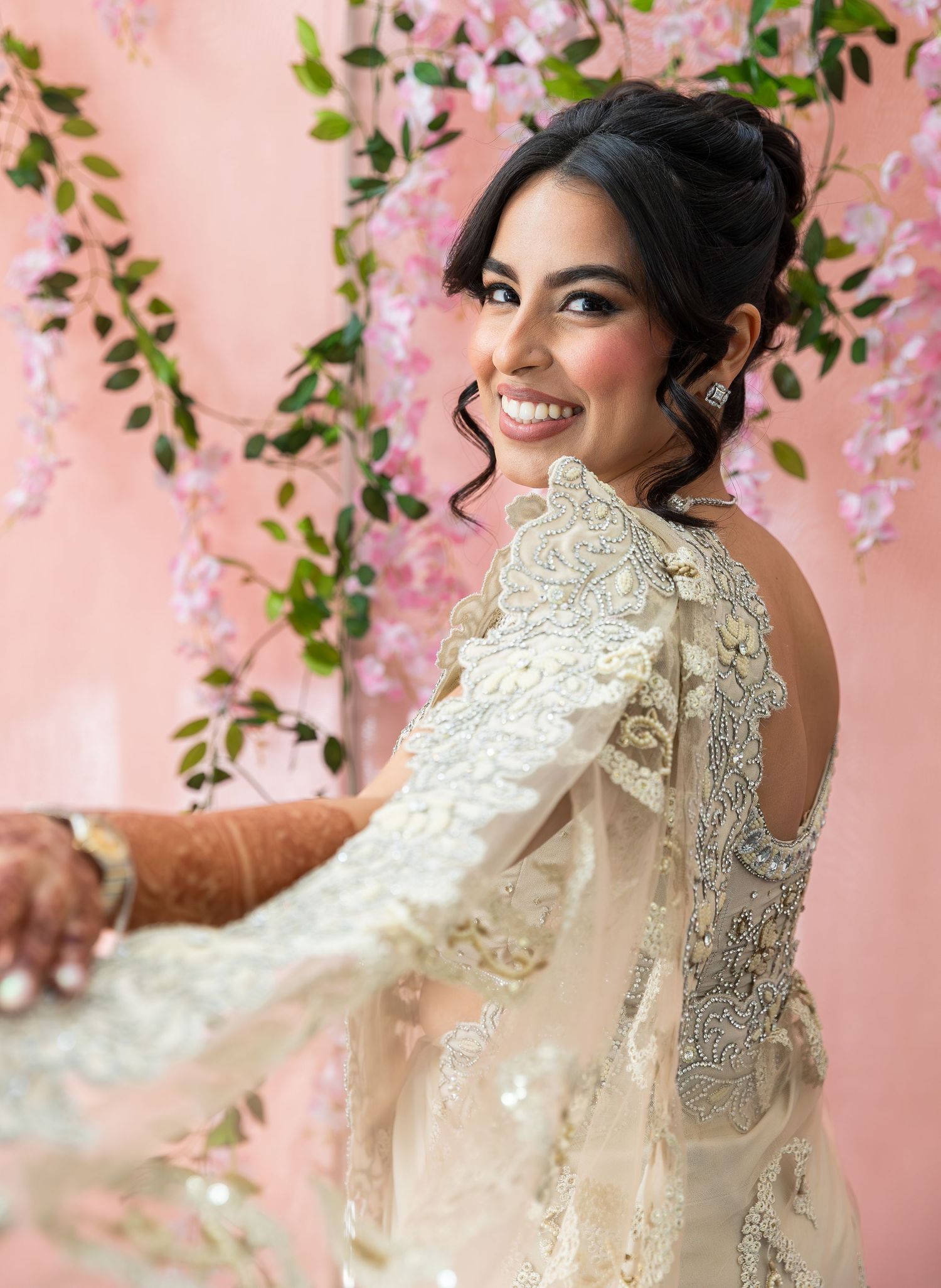 Wedding portrait with lace dress details against a pink floral backdrop.
