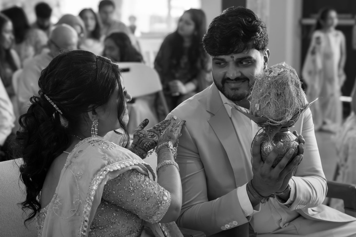 A couple shares a joyful moment at a wedding celebration as they interact with a small dog in black and white photography.