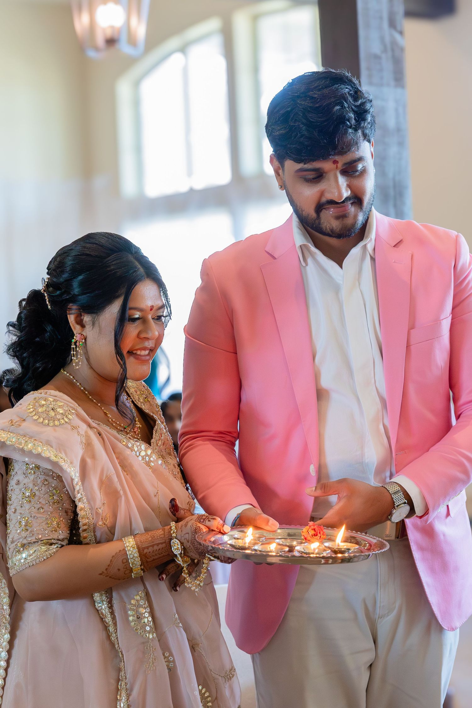 A series of four photos showing a couple lighting and blowing out birthday candles while wearing pink and gold attire.