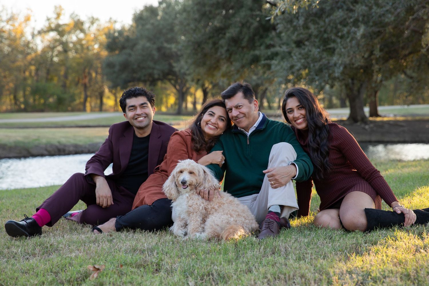 Family and dog relaxing together on grass during golden hour in a park setting.