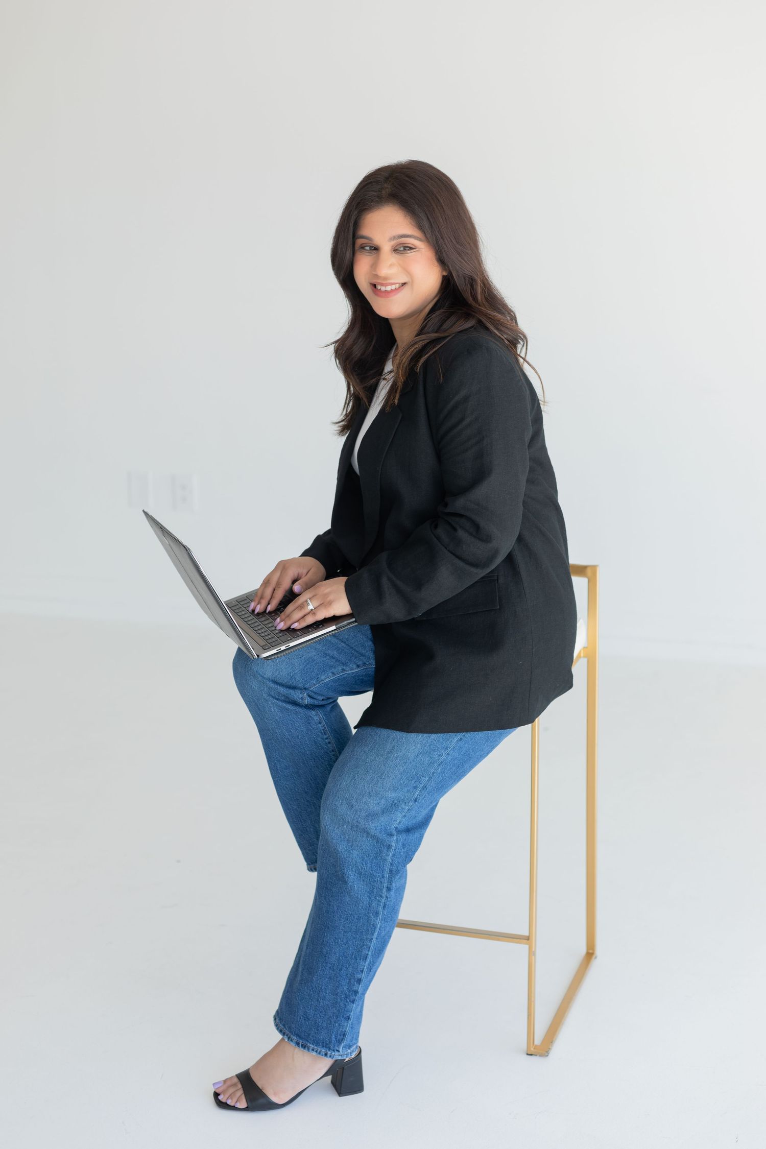 Business professional working on laptop while seated on minimalist gold chair.