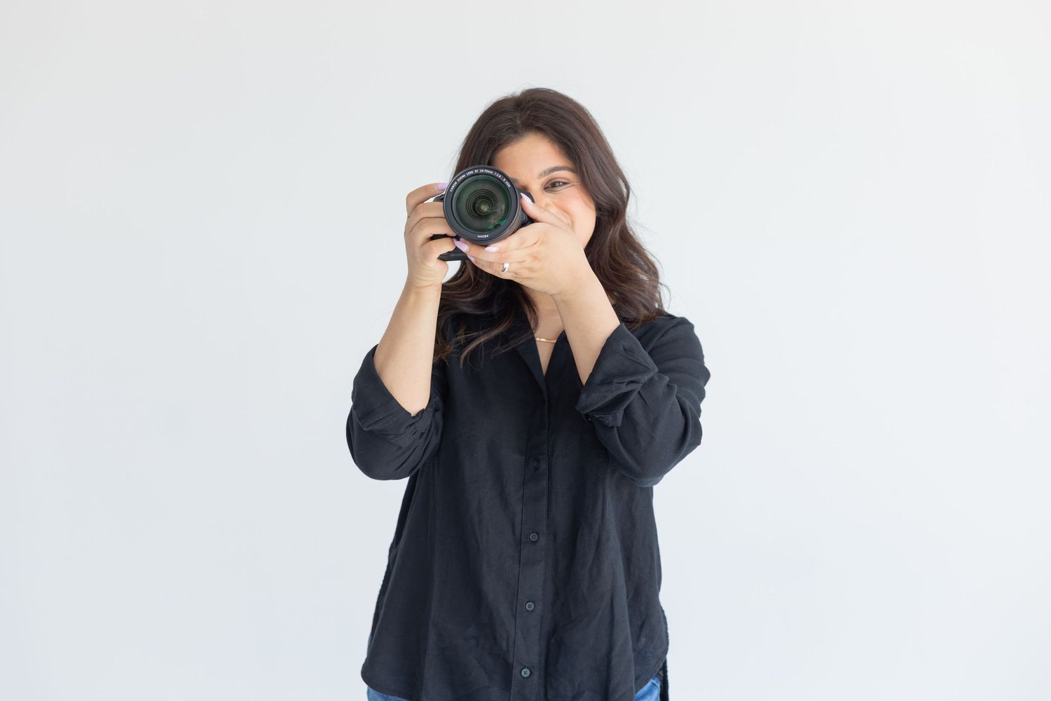 Photographer in black shirt taking picture with professional camera against white background.