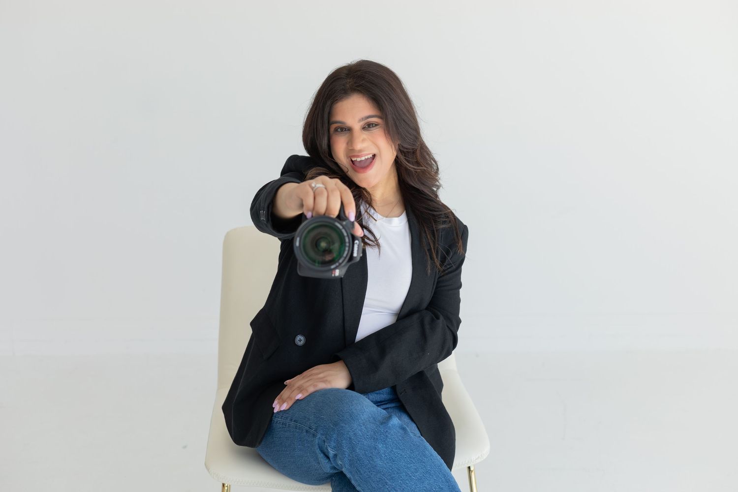 Photographer in casual business attire poses with camera in studio setting.
