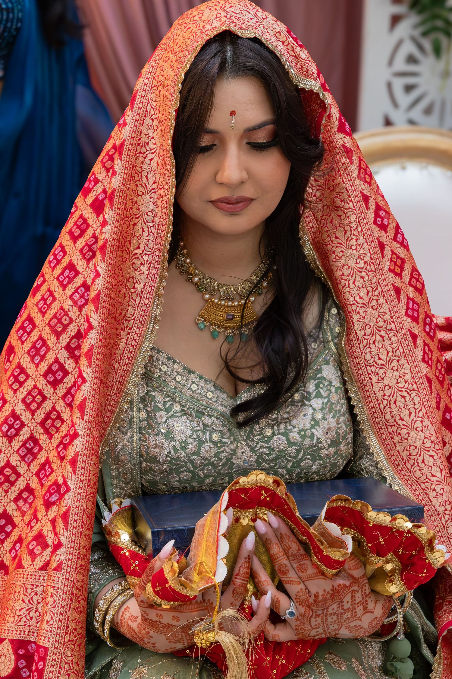 Traditional Indian bride wearing ornate red and gold dupatta and intricate bridal jewelry during wedding ceremony.