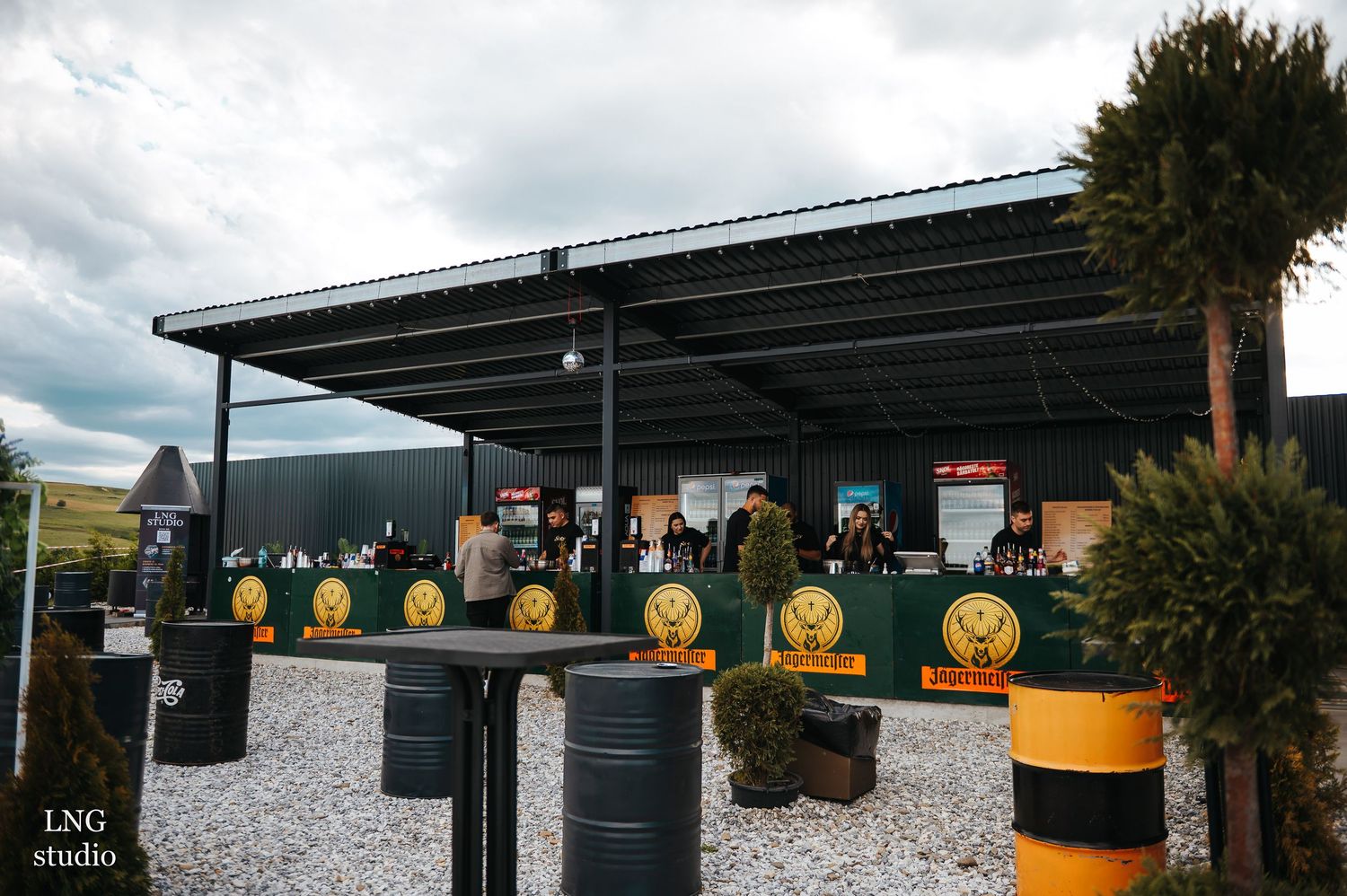 Outdoor venue setup with yellow barrels and structures under cloudy sky.