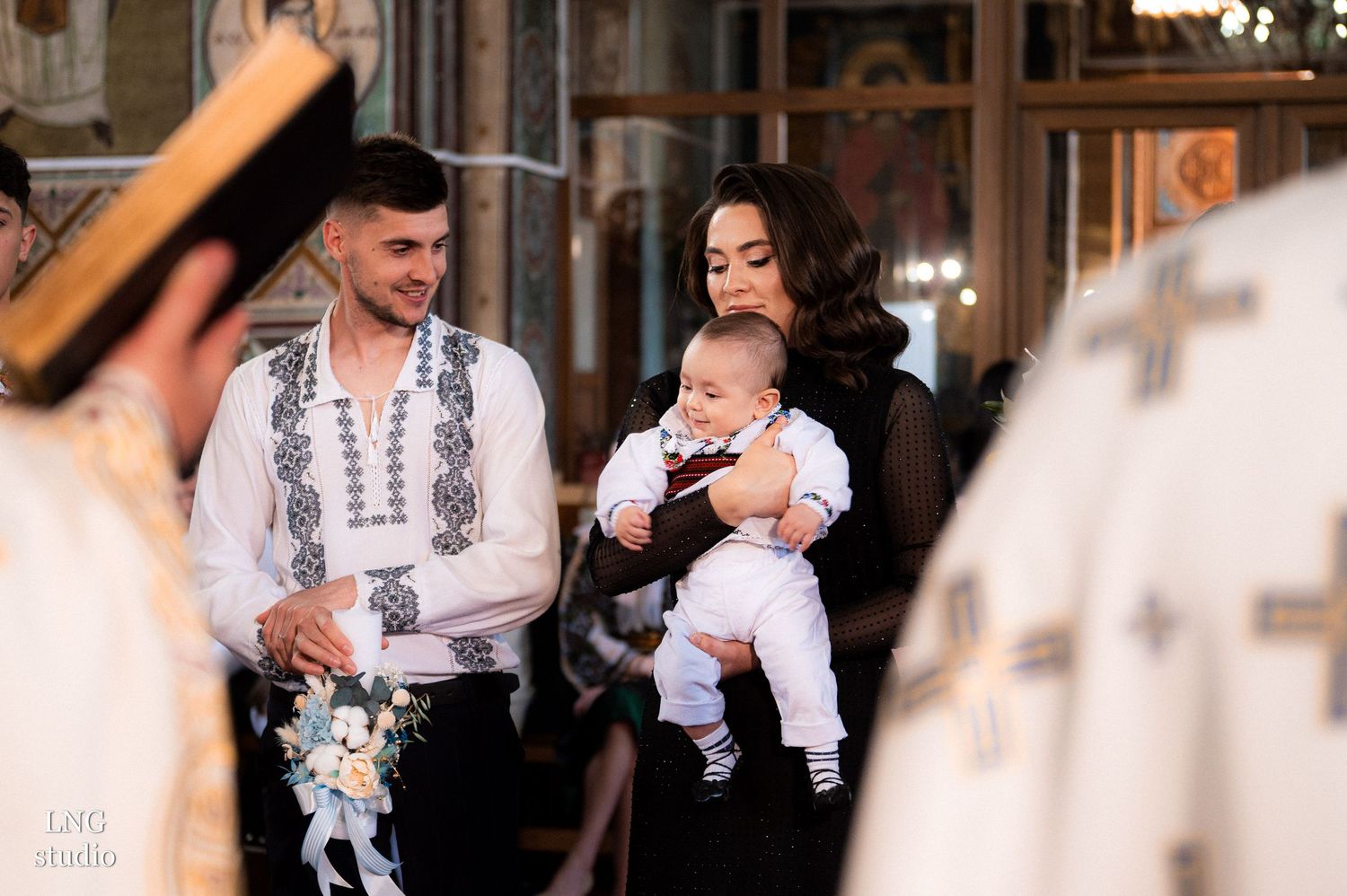 Orthodox baptism ceremony showing traditional embroidered clothing in a church setting.