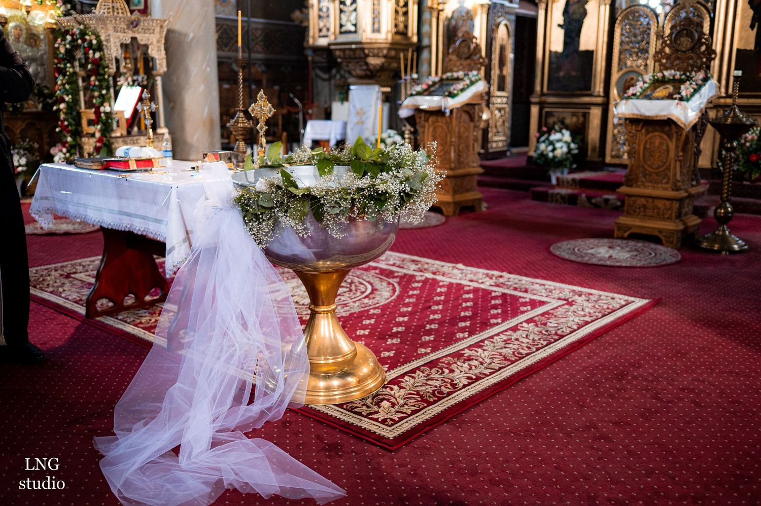 Orthodox church altar decorated with white tulle, flowers and red carpet for ceremony.