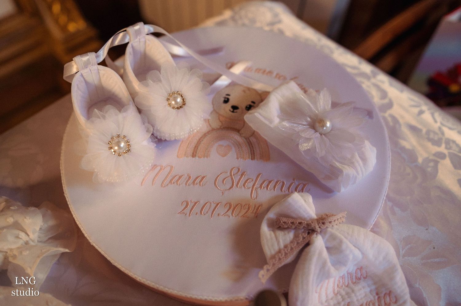 White infant baptism shoes with floral details displayed on personalized ceremonial paper.