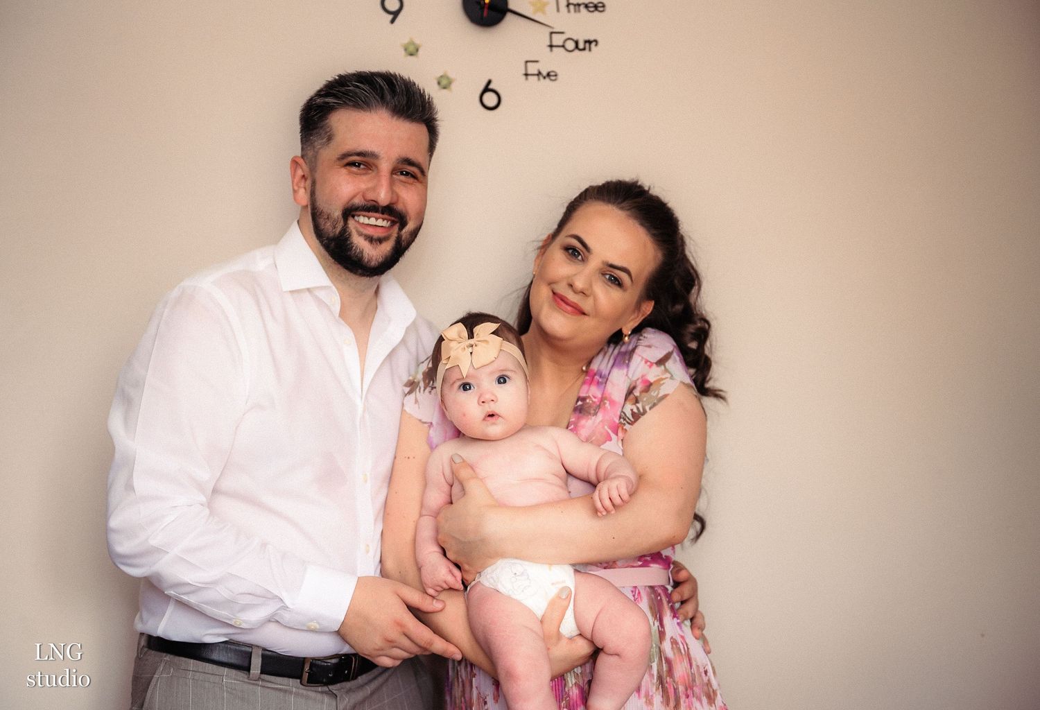 A family poses together for a portrait against a neutral wall with clock decorations.