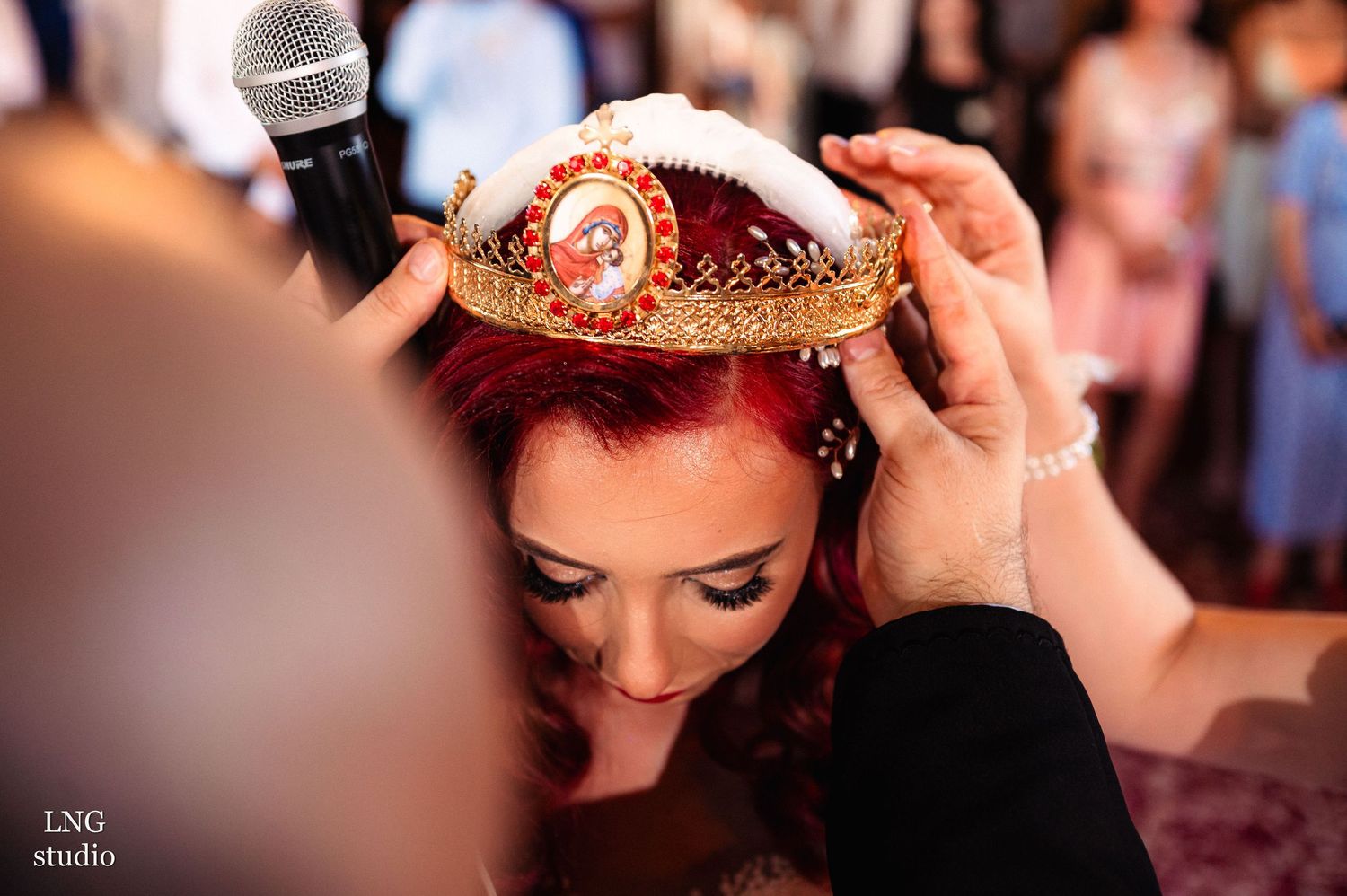 Ornate crown being placed on red-haired bride during wedding ceremony.