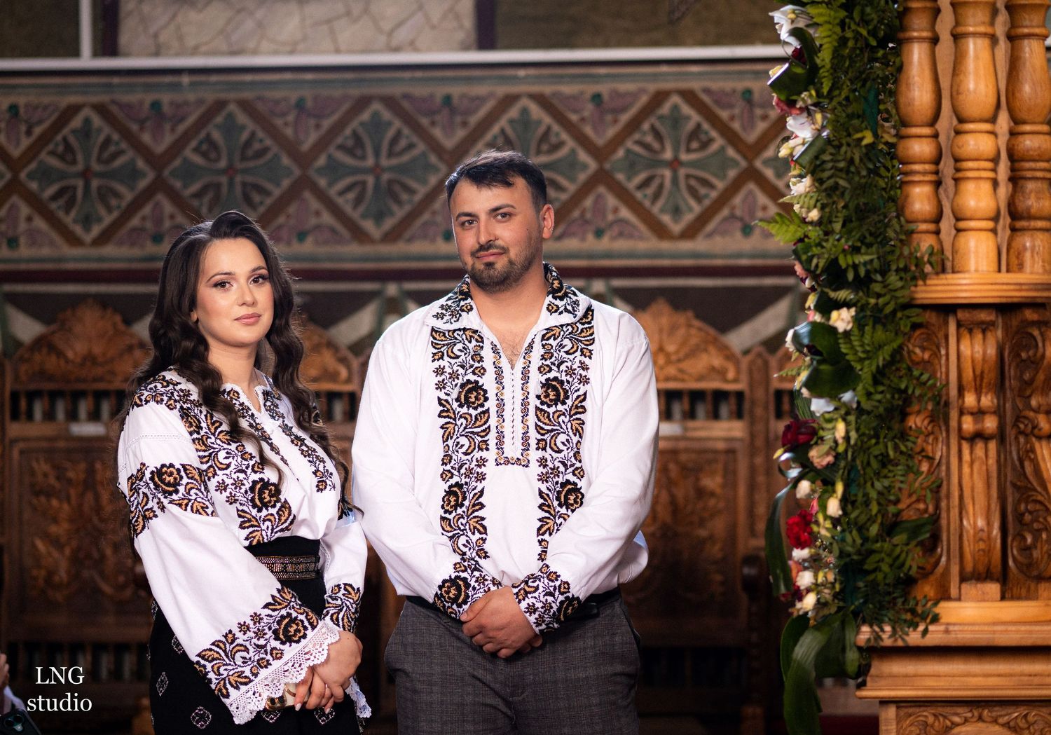 Couple wearing traditional Eastern European embroidered clothing in church interior.