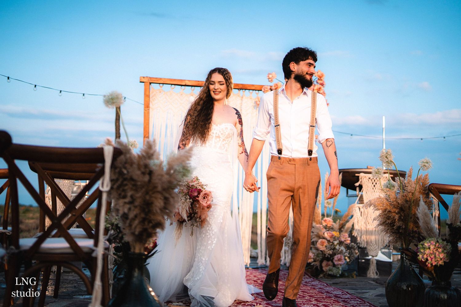 Couple dancing at a beachside wedding celebration with string lights and ocean views at sunset.