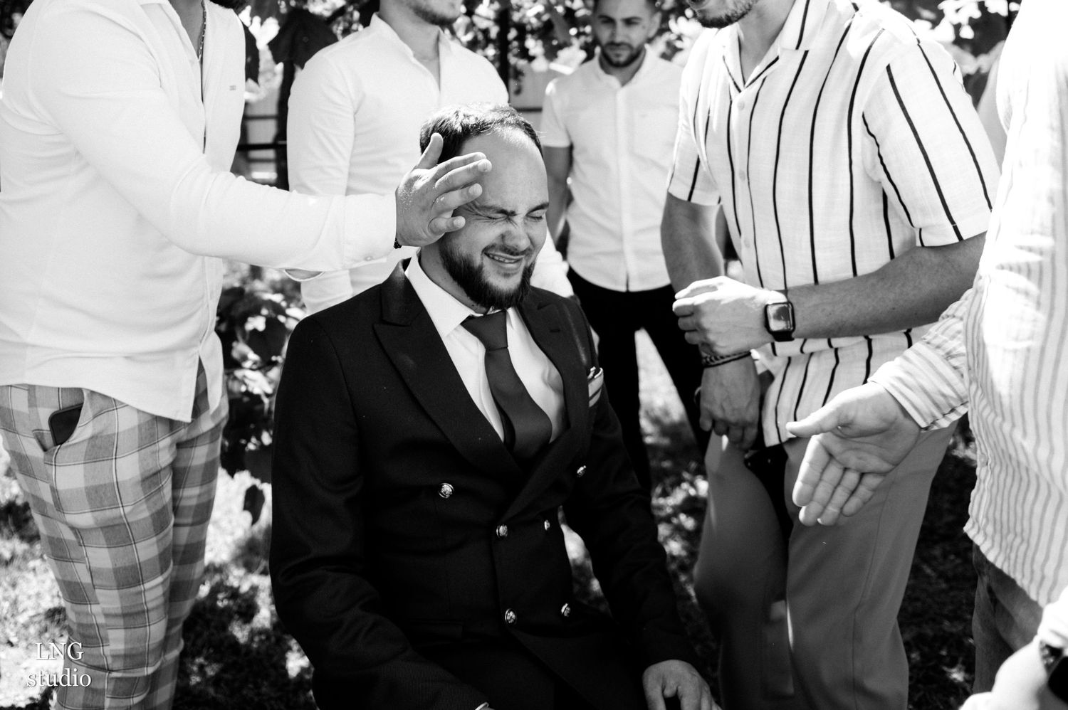 Black and white candid moment of groomsmen preparing for wedding day celebrations.