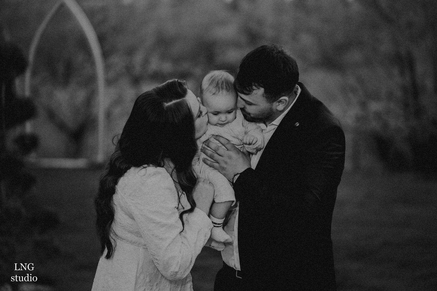 Black and white portrait of a tender family moment outdoors in a garden setting.