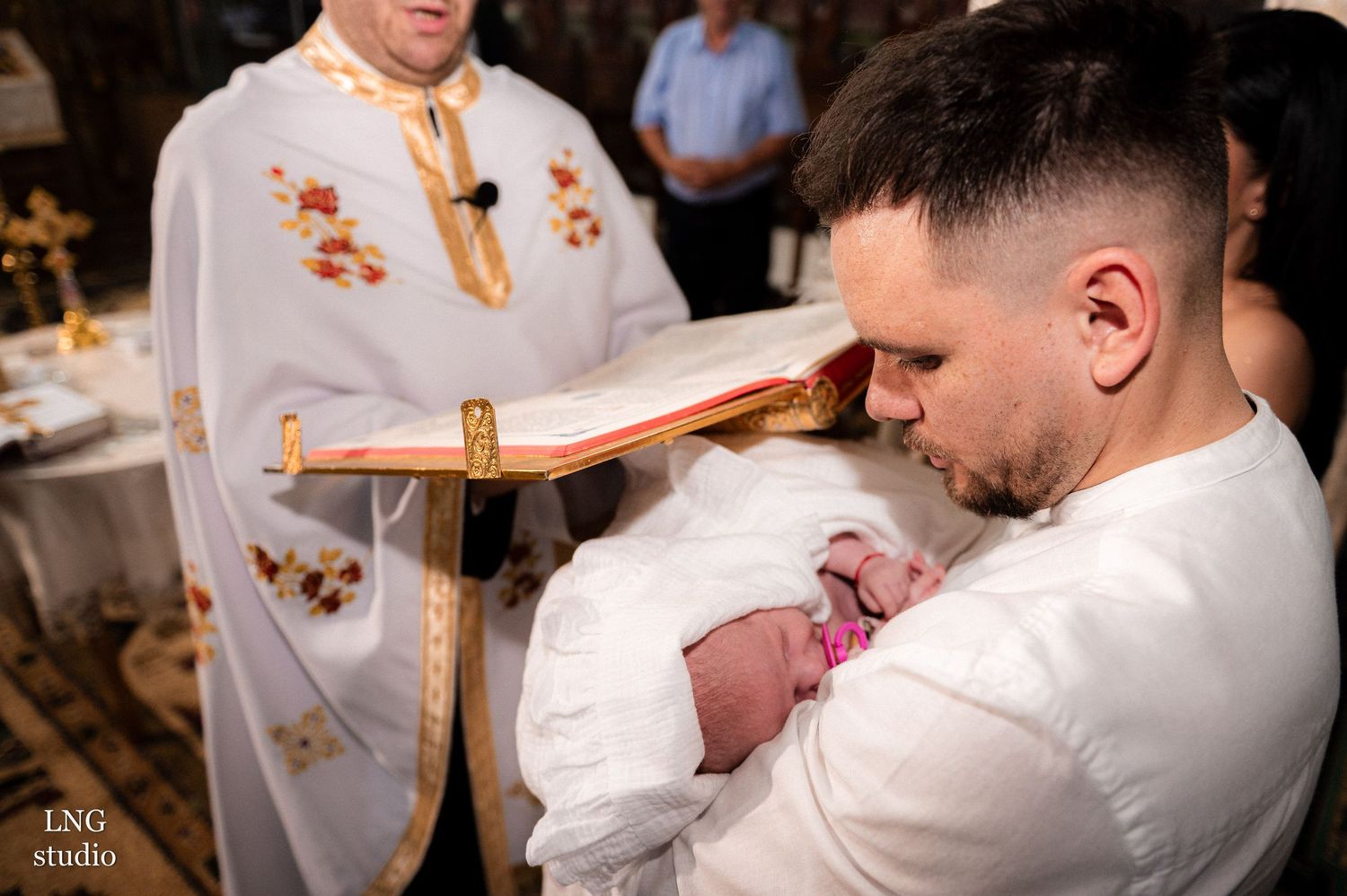 Intimate moment during Orthodox Christian baptism with white robes and cross.