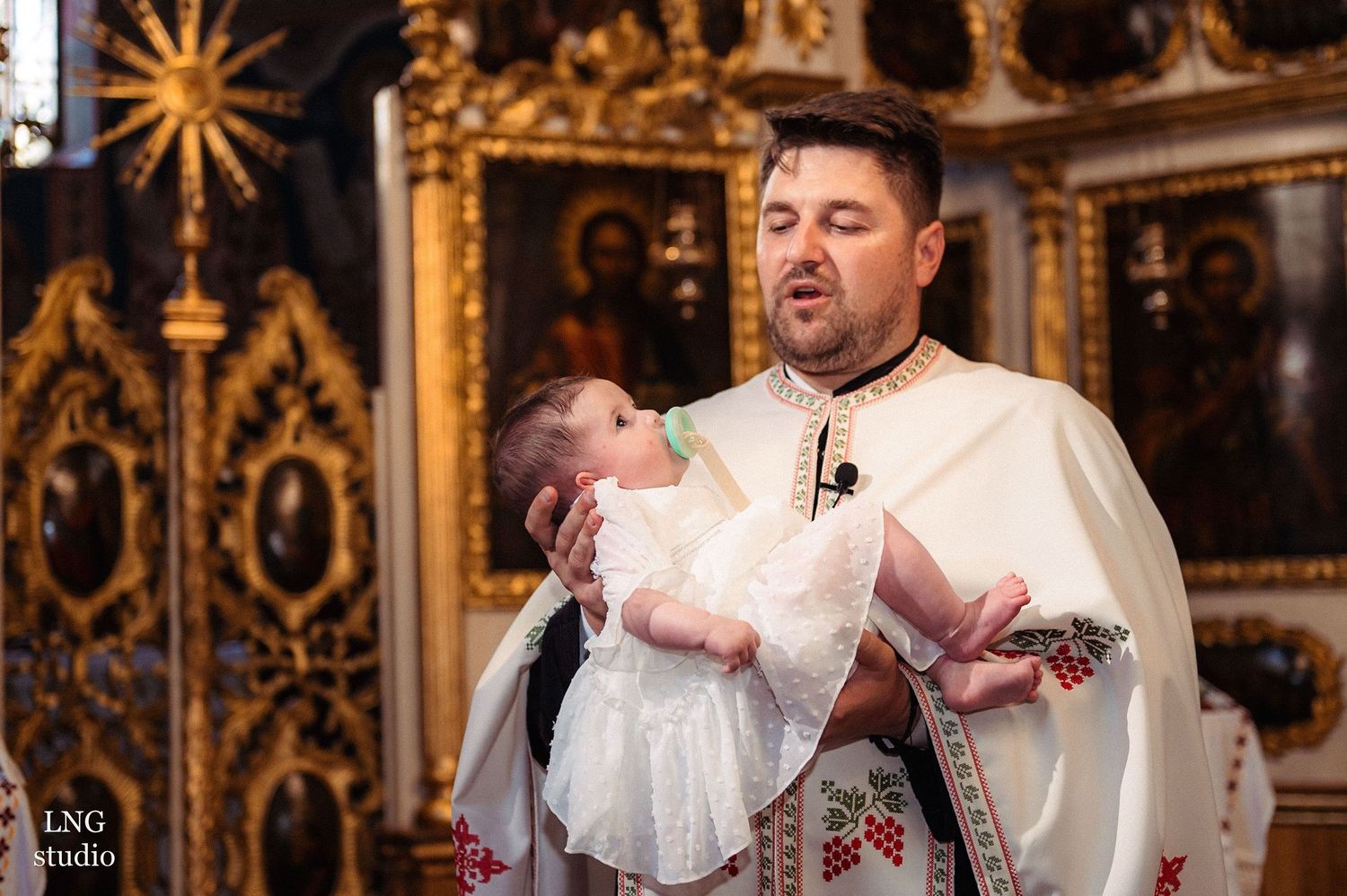 A traditional baptism ceremony taking place in an Orthodox church with golden iconostasis.