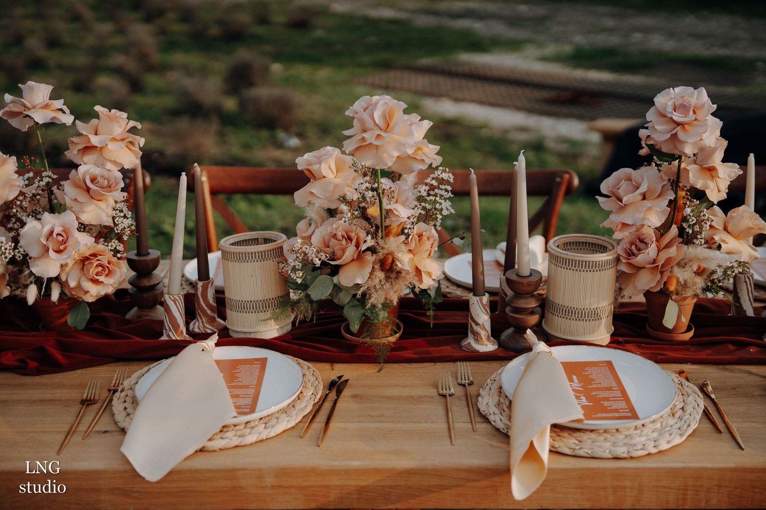 Elegant floral arrangements with pink and white roses along rustic wooden tables create a romantic wedding reception setting.
