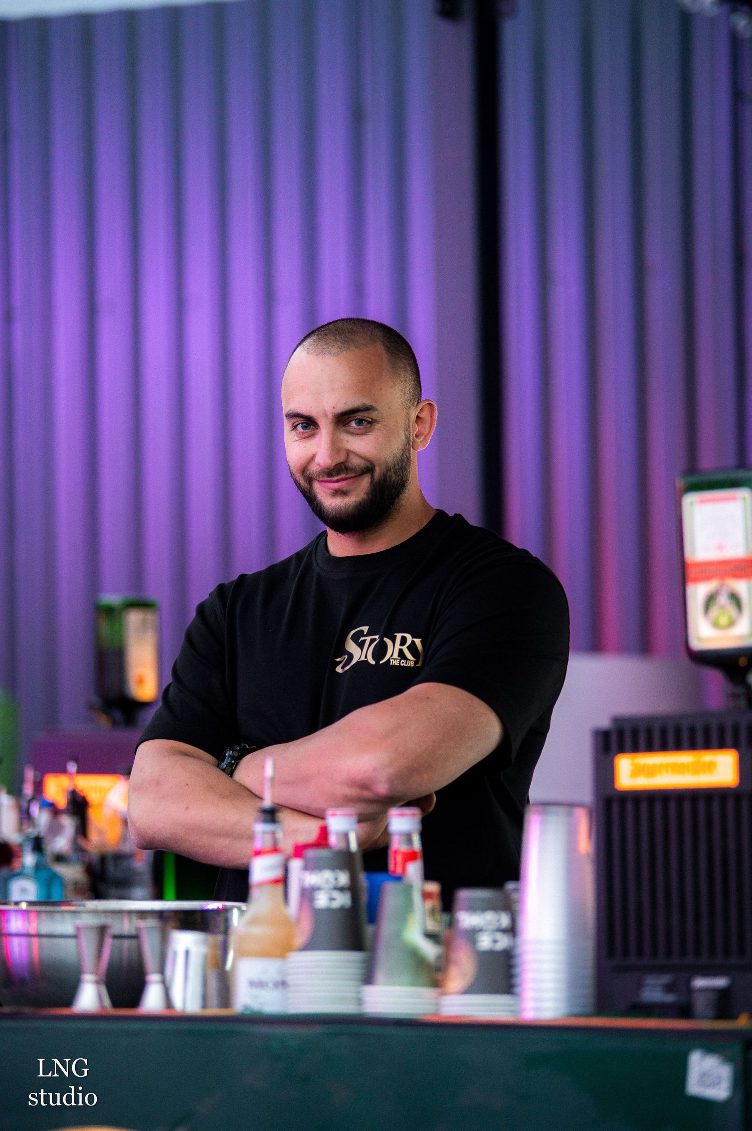 Bar staff members smiling and gesturing while working at an illuminated service counter.