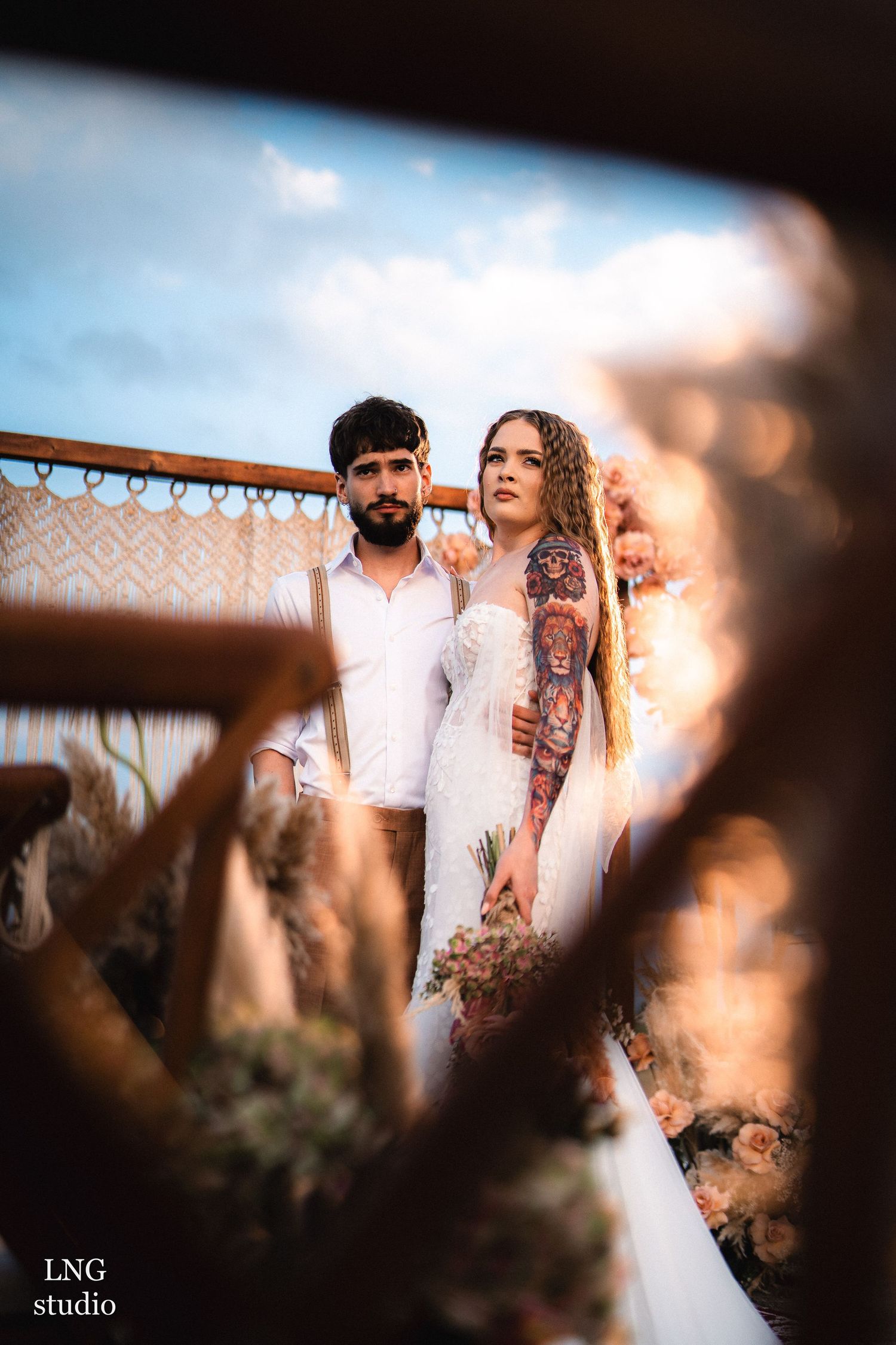 Artistic wedding photo showing a tattooed couple standing together against a golden sunset backdrop.
