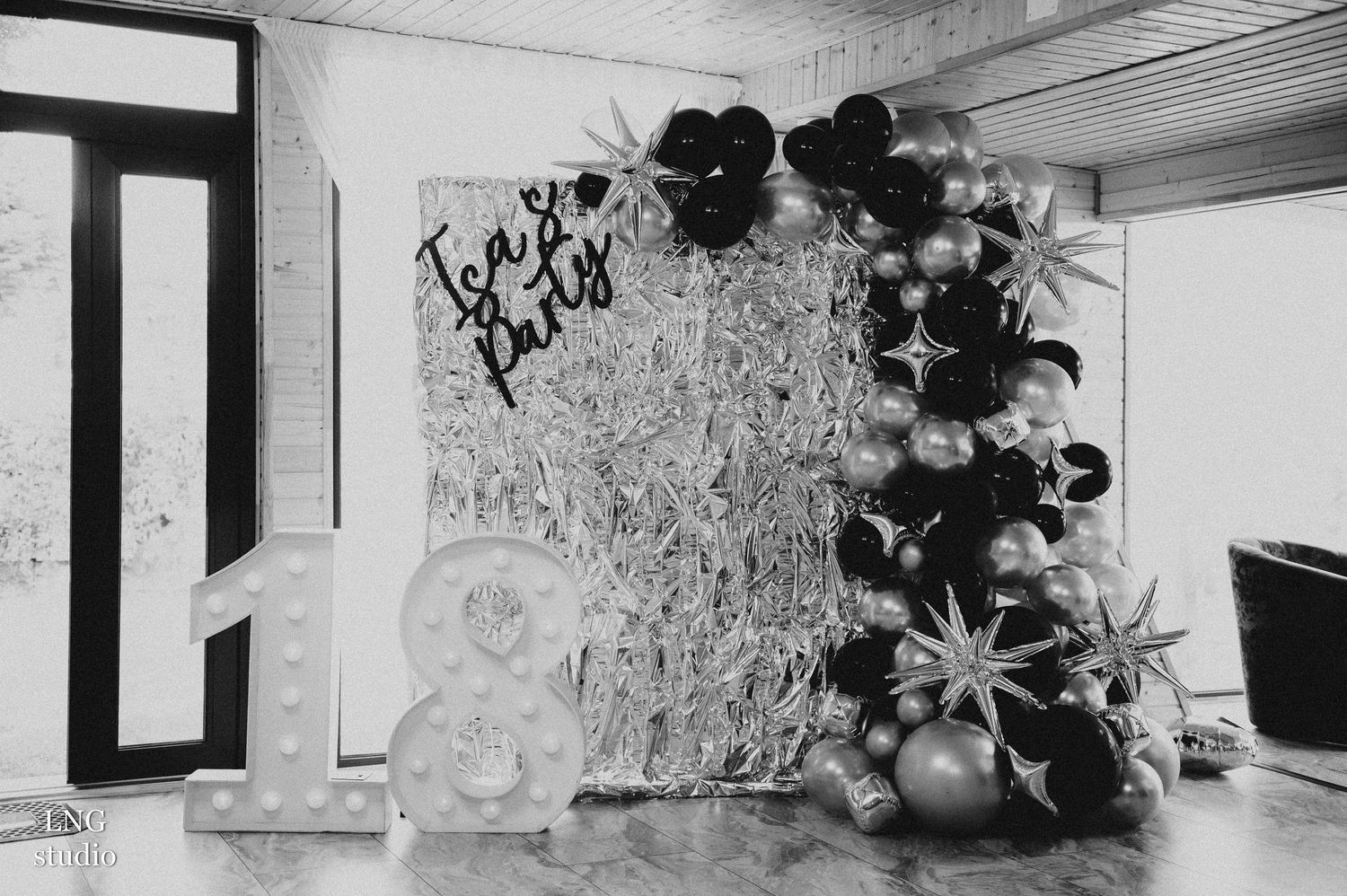 Black and white photograph of a decorative corner display with balloon arch and sculptural elements.