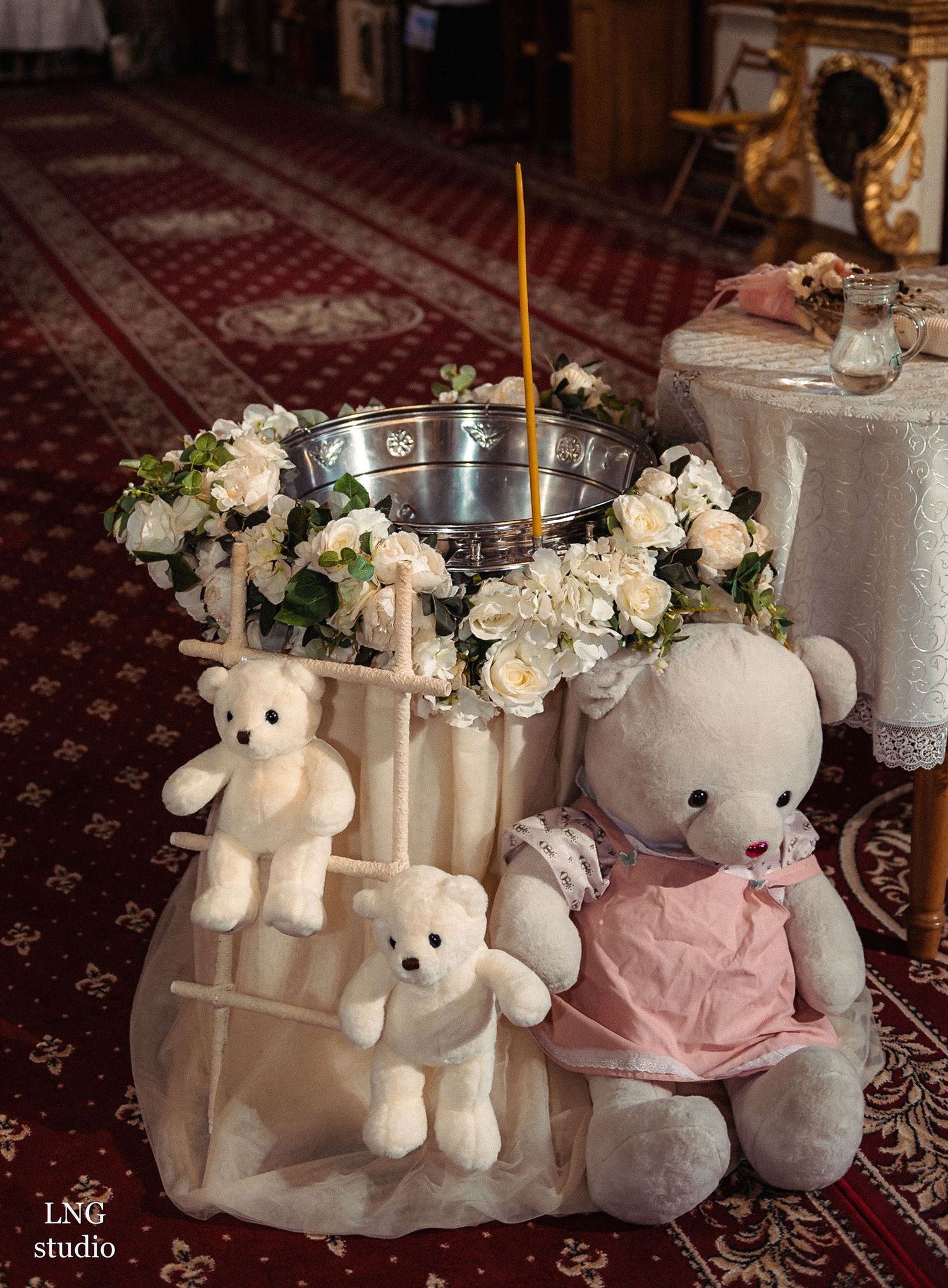 Decorative teddy bears and white floral arrangements surround a silver bowl on an elegant table setting.
