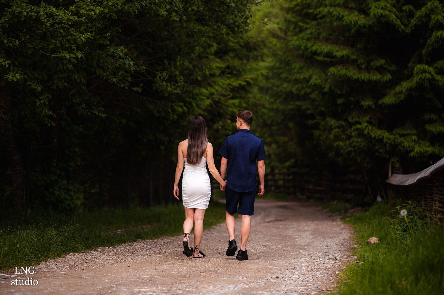 Intimate couple moment captured on natural pathway surrounded by evergreen trees.