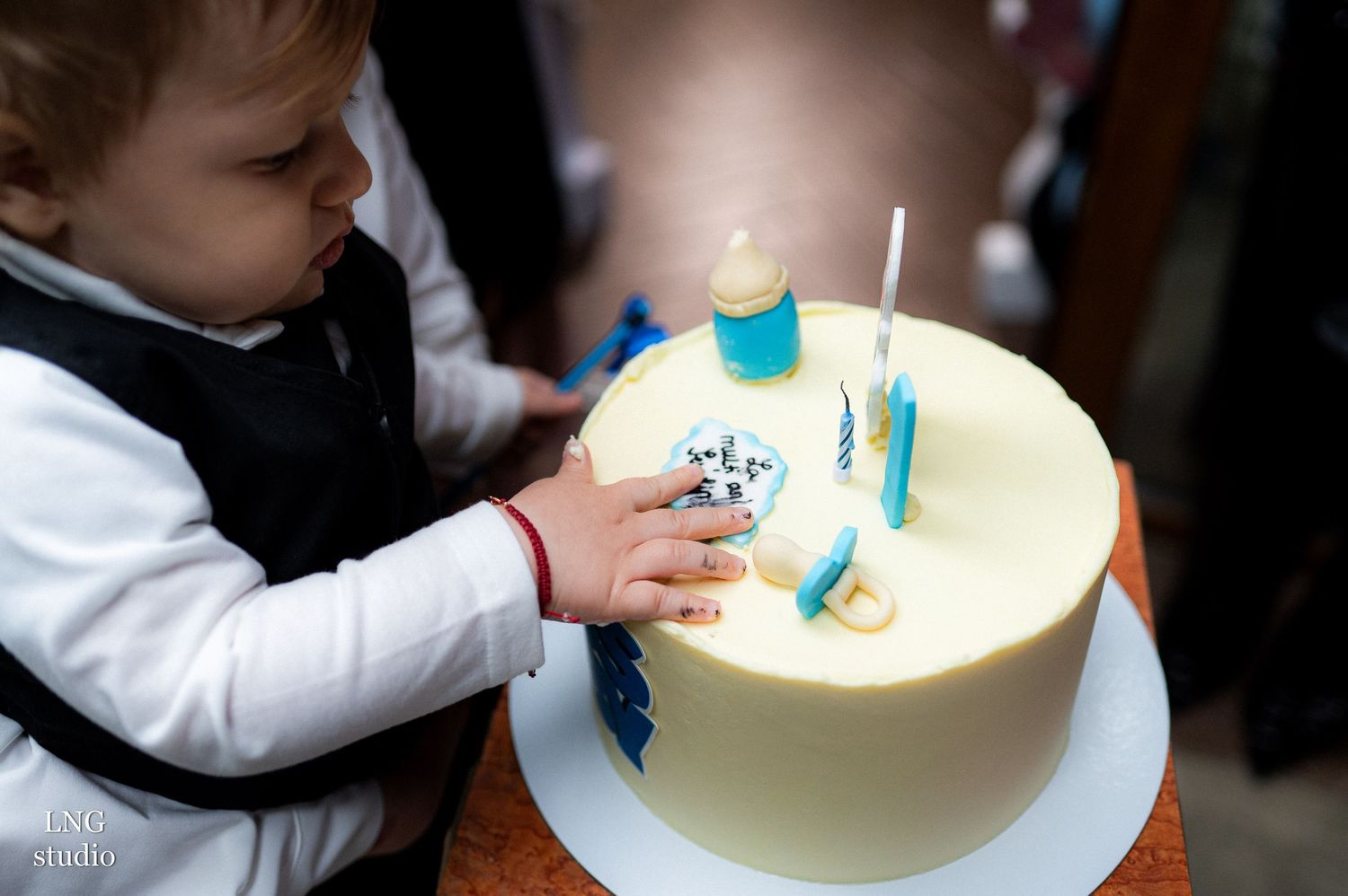 Small hands reaching for decorations on a white birthday cake.