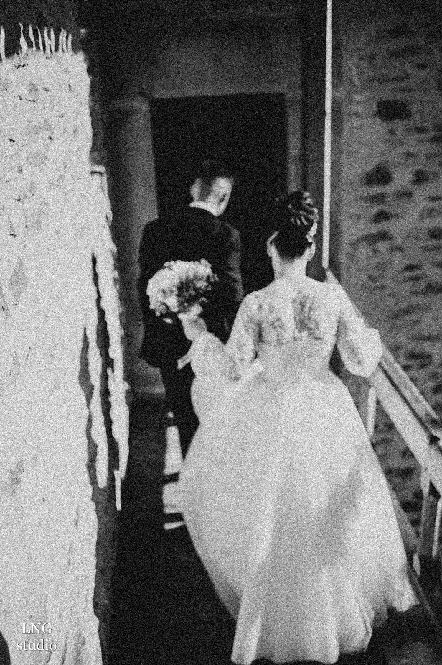 Newlywed couple walking through stone doorway in vintage black and white photography.