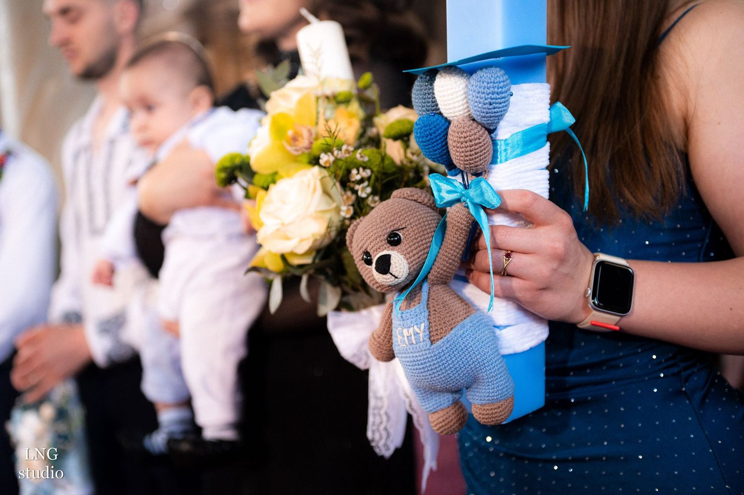 Decorative blue baptism candle with teddy bear and yellow flower bouquet.