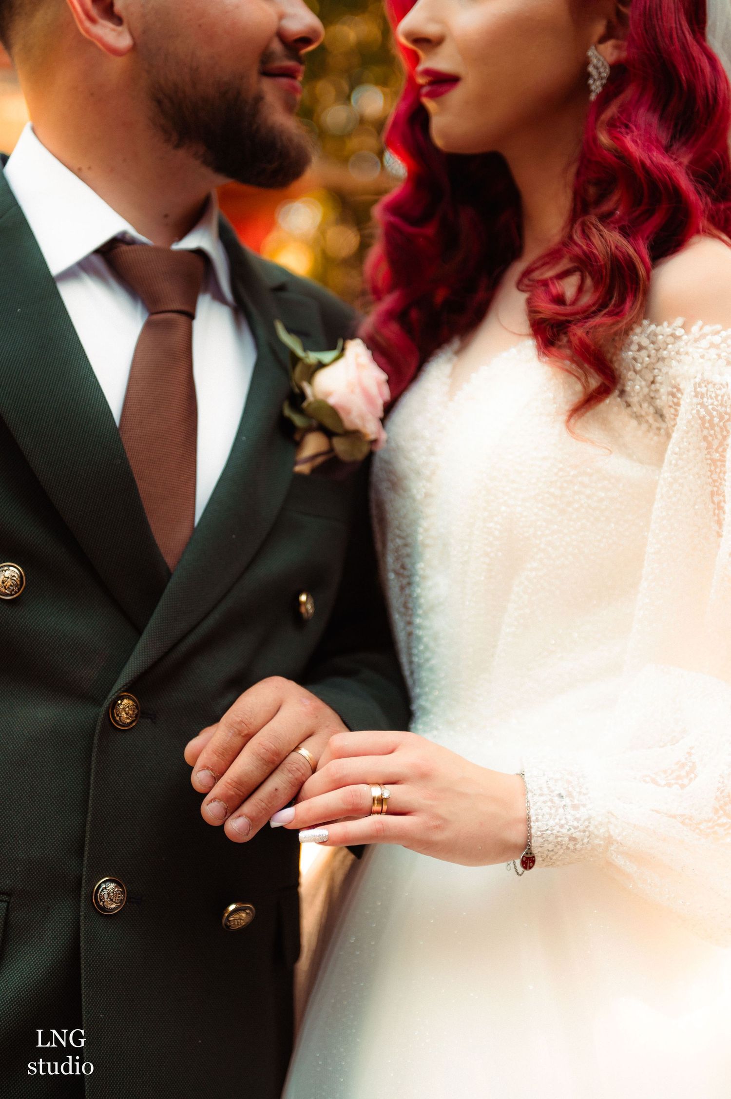 Close-up of couple's wedding attire showing a dark military style suit and white lace dress with vibrant red details.