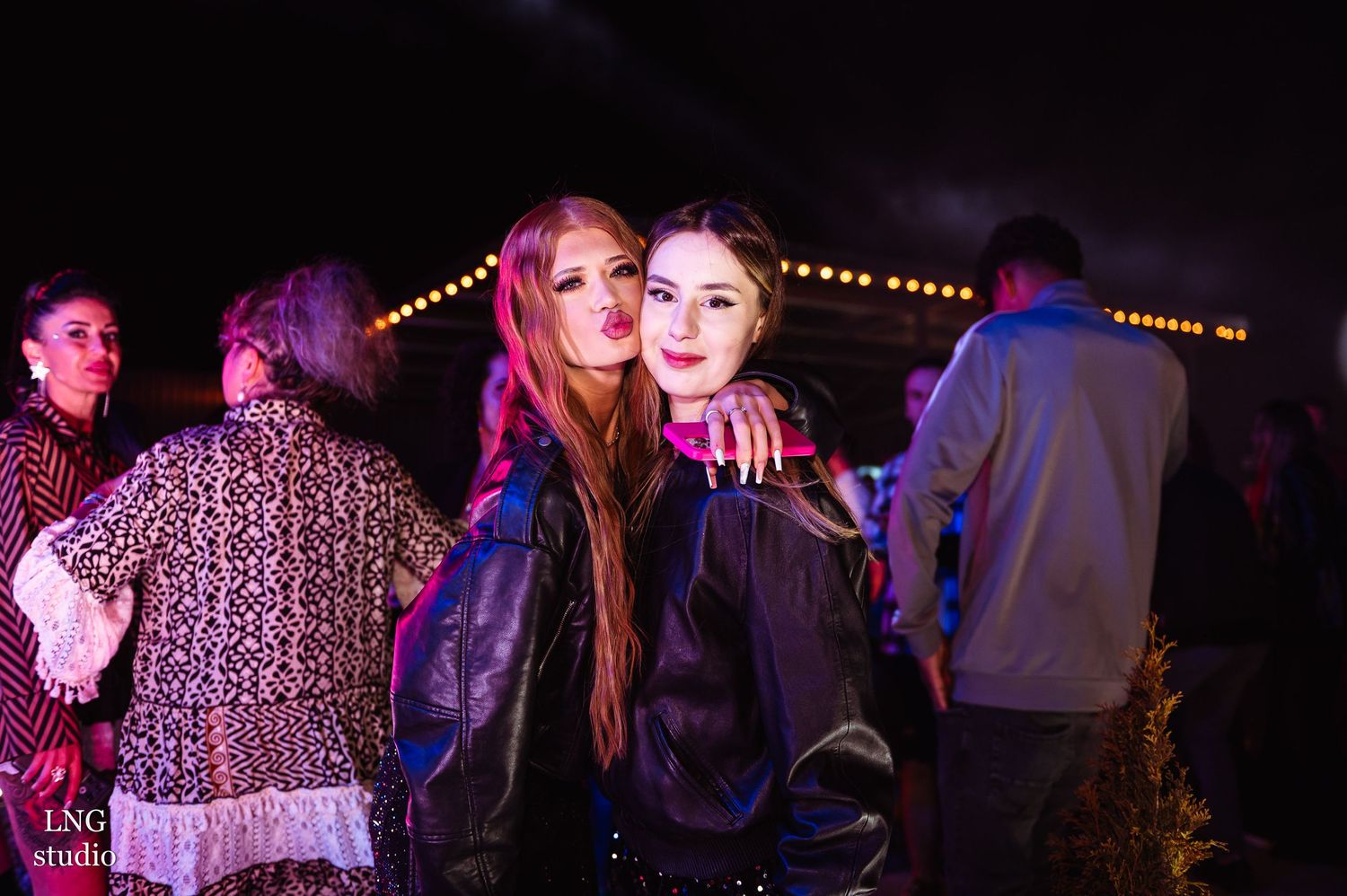 People enjoying a nighttime event under purple lighting and decorative string lights.