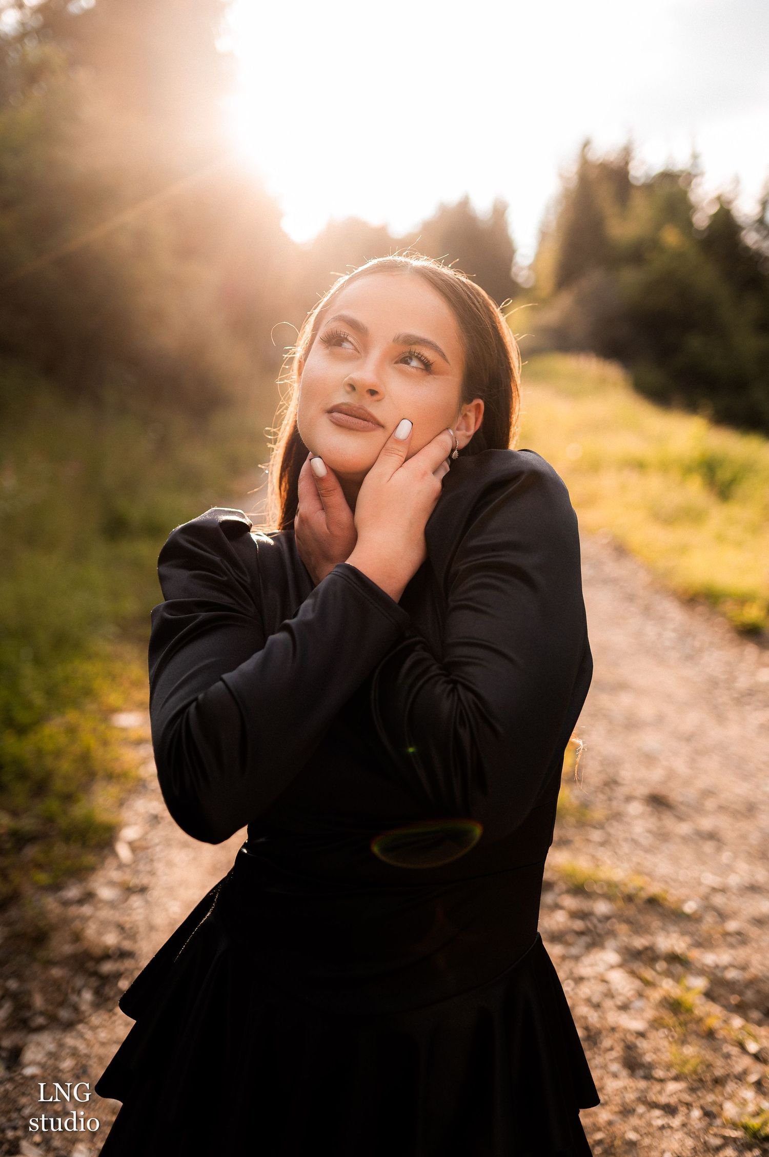A person in a black coat poses thoughtfully on a sunlit path with golden bokeh background during golden hour.