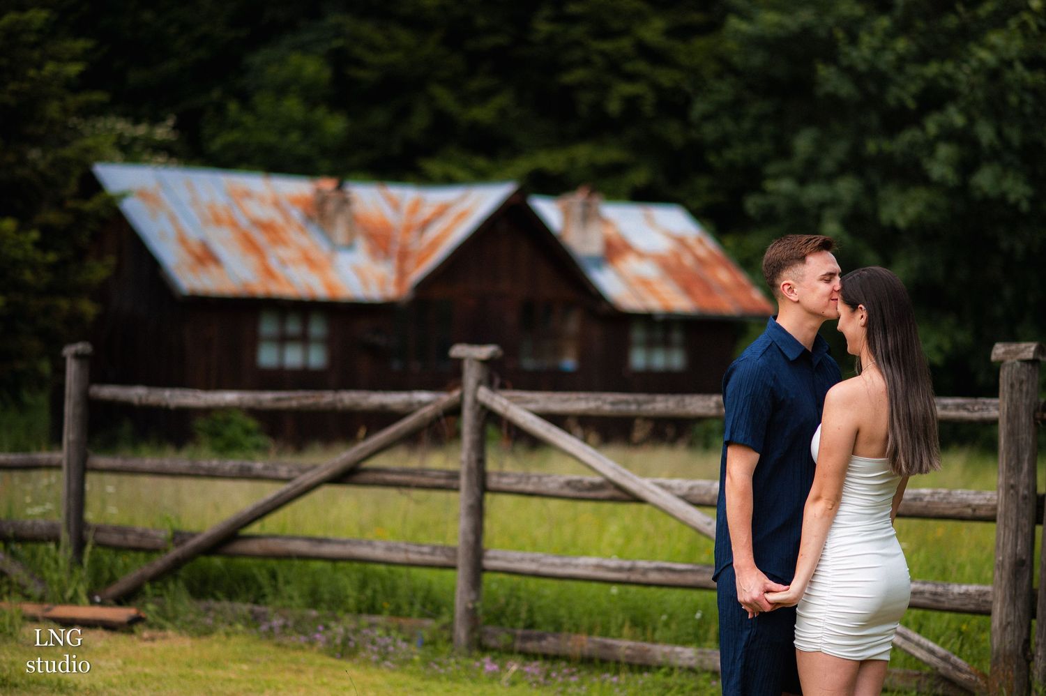 Couple poses intimately near rustic cabin in mountain landscape.