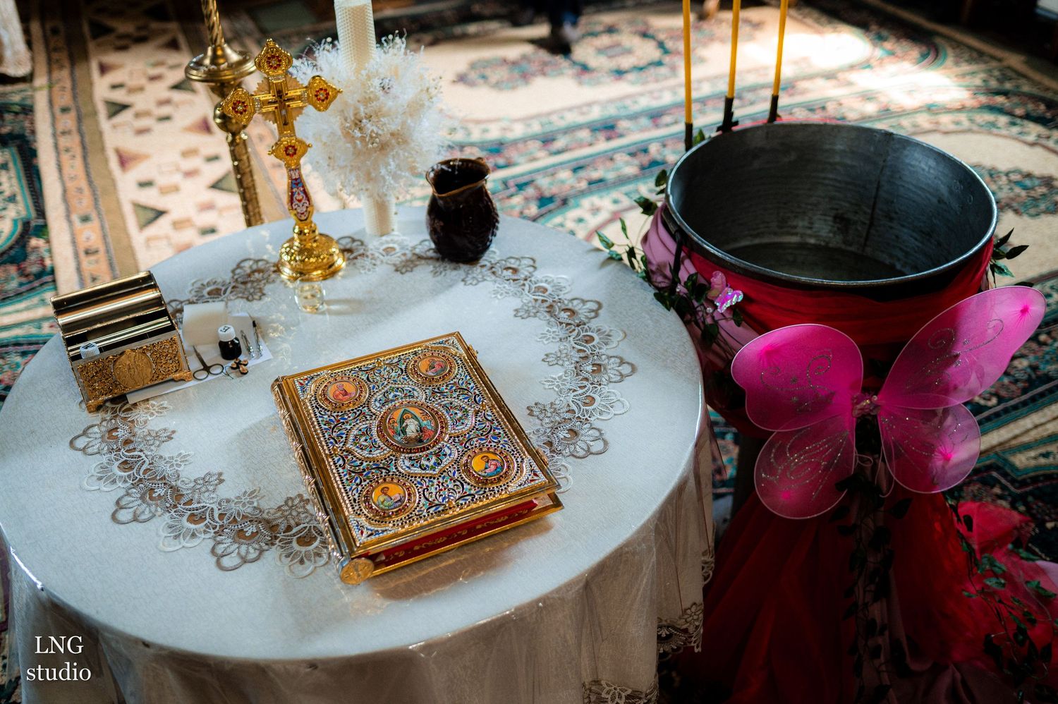 Decorated table setting with religious book, cross, and pink accessories for a ceremony.