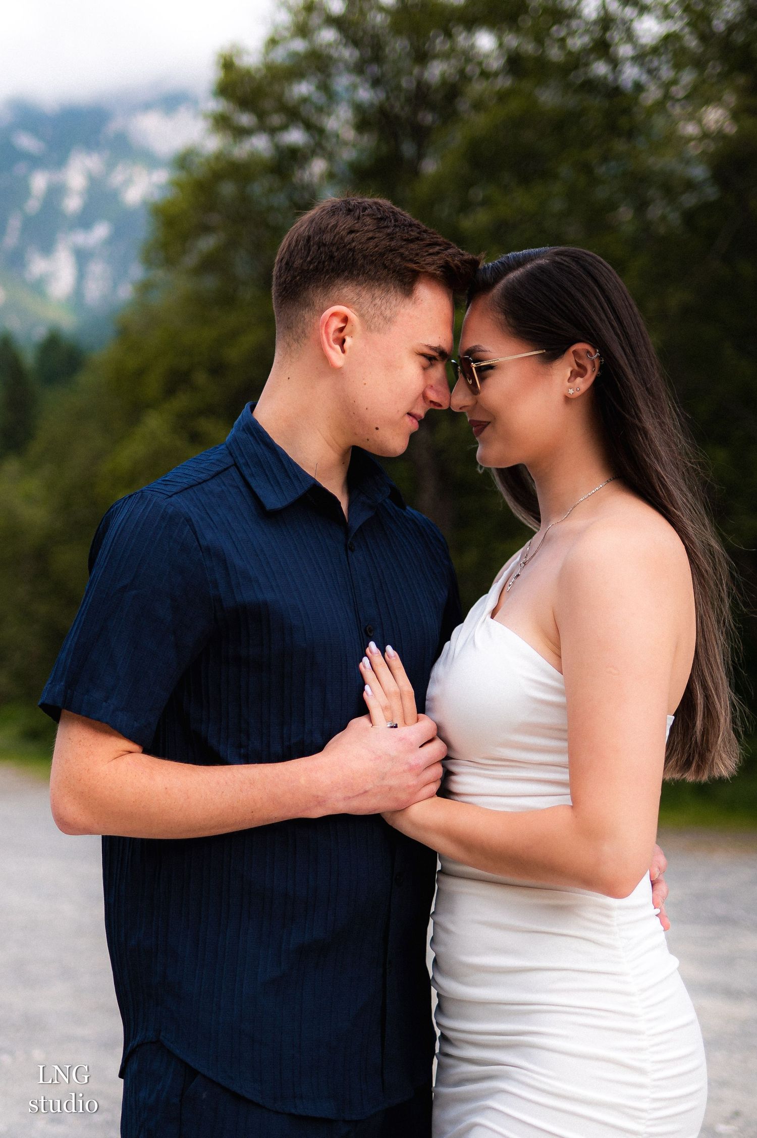 Couple in navy and white outfits share tender moment outdoors.