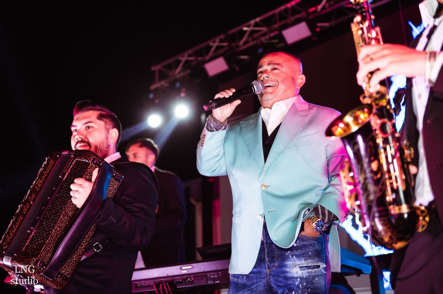 Performers on stage singing and playing instruments during a lively musical concert performance with colorful lighting.